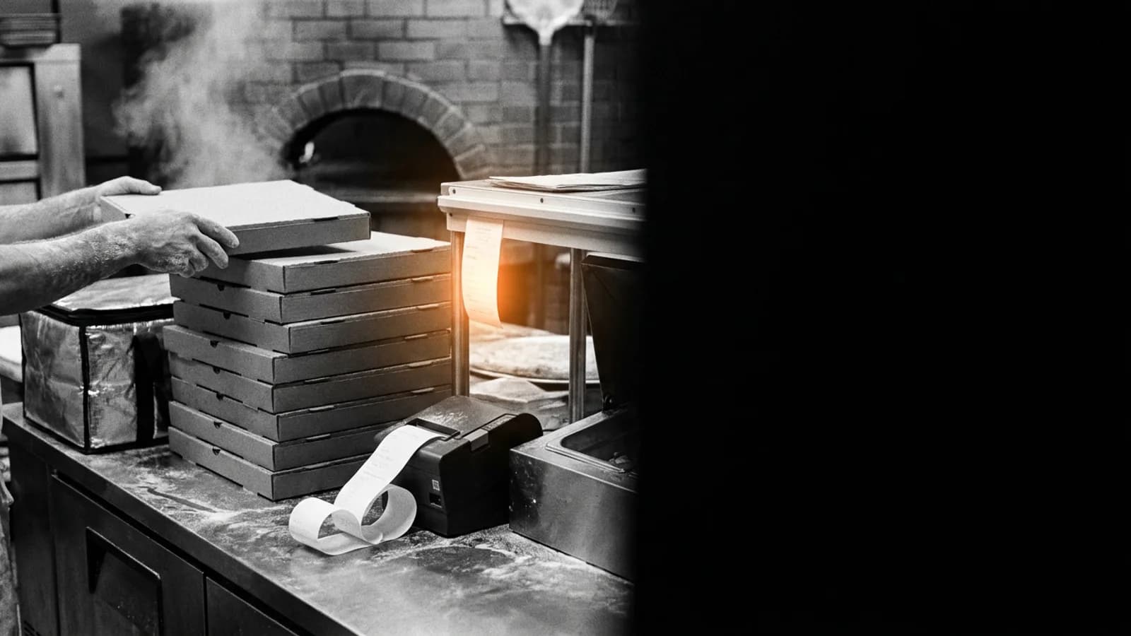 Los pedidos apilándose en Pa'Comer Una pila de cajas de pizza cerradas en el pase de una pizzería cubana con el riel de comandas al lado y una encendida en naranja